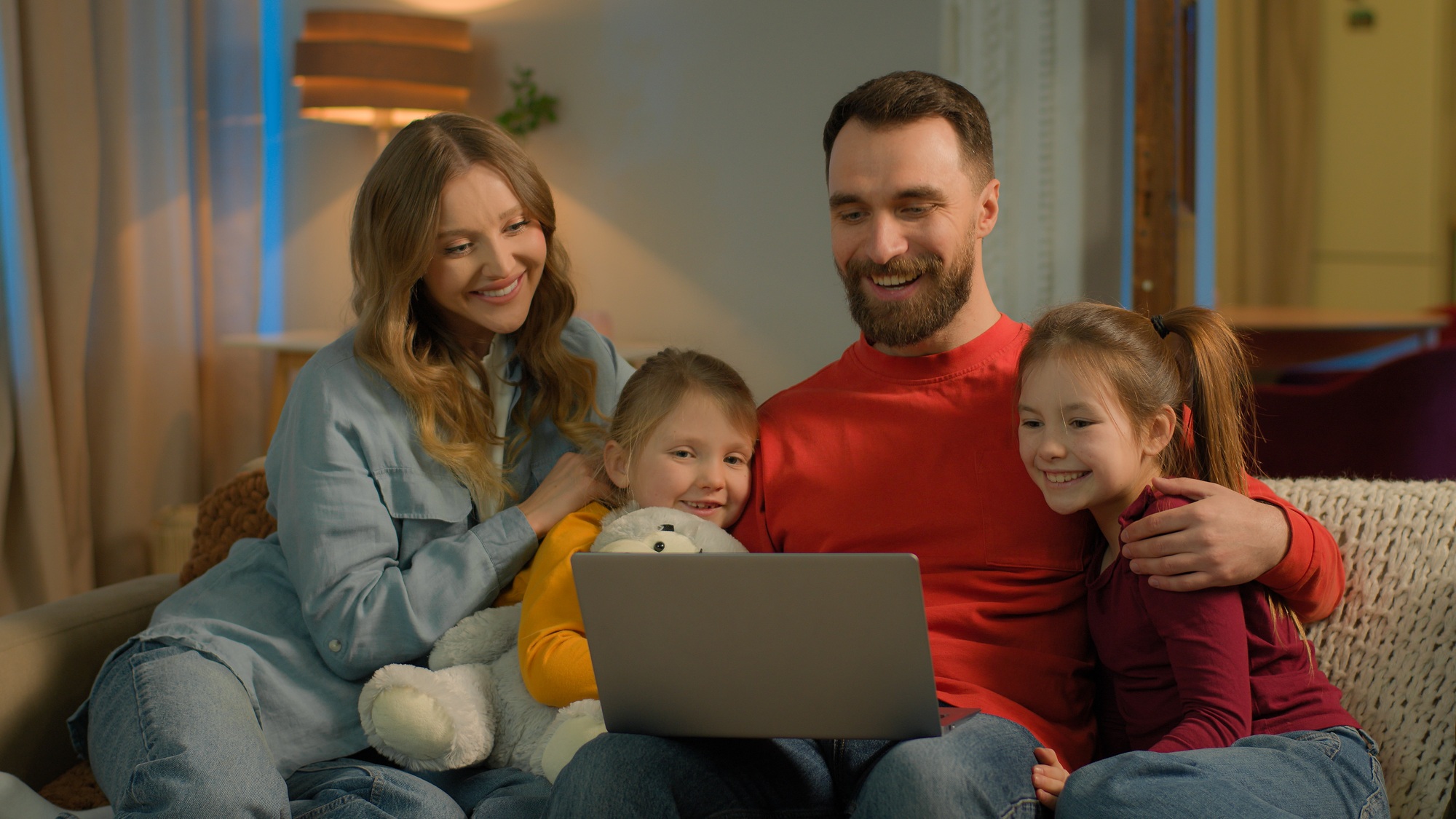 Caucasian family parents children on couch evening home teach little girls using pc laptop mom dad